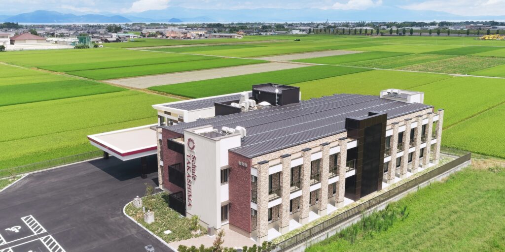 広大な田園に囲まれた介護施設の建物全景。赤レンガと白のモダン建築。